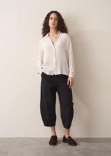 Woman wearing a white silk shirt and black trousers against a plain background