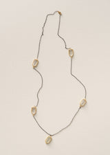 A delicate geometric statement necklace featuring five irregular, elongated gold-toned pendant shapes set in a thin silver-toned chain, displayed flat against a textured off-white background.