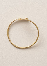 A hammered gold open cuff bangle bracelet with a small clear gemstone accent on each end, displayed on a textured off-white background.
