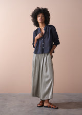 Woman wearing a dark blue button-up shirt and striped trousers against a beige background
