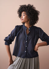 Woman wearing a navy blue blouse with striped trousers, against a beige background