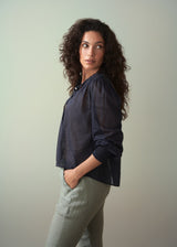 Woman wearing a light cotton navy blouse with ruched cuffs, paired with green trousers