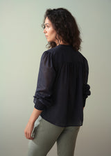 Woman wearing a light cotton navy blouse with ruched cuffs, paired with green lightweight trousers