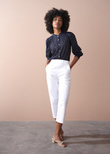 Woman wearing a light cotton navy blouse with ruched cuffs, paired with white trousers and sandals