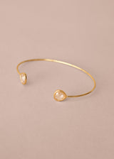 Gold bracelet with two clear gemstones on a beige background