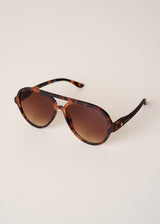Tortoiseshell sunglasses with brown gradient lenses on a light beige background