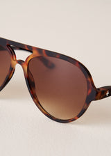 Tortoiseshell sunglasses with brown lenses on a light beige background