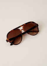 Sunglasses with tortoiseshell frame and brown lenses on a light beige background