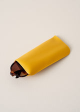 Yellow glasses case with a pair of sunglasses peeking out on a beige background