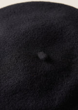 Close-up of a black felt or wool beret hat showing the soft textured surface and a small central dimple.