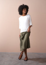 Woman wearing a white top and green satin midi skirt against a beige background