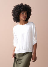 Woman wearing a white top and green satin midi skirt against a beige background