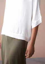 Person wearing a white satin top and green satin midi skirt on a plain background