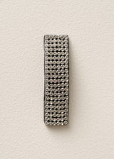 A rectangular black wristband or bracelet covered in rows of clear rhinestones, displayed vertically against a textured off-white background.