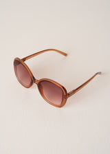 Brown sunglasses with a gradient lens on a light beige background