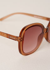 Brown sunglasses with a visible brand logo on a light background