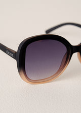 Black sunglasses with gradient lenses on a light beige background