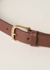 Brown leather belt with a brass buckle on a beige background
