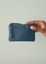 Hand holding a blue leather pouch against a light gray background