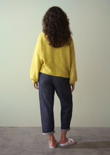 Woman wearing acid yellow knit cardigan with bow tie front, paired with navy trousers