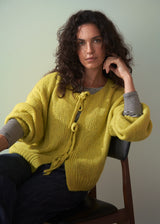 Woman wearing acid yellow knit cardigan with bow tie front over a stiped long sleeve top