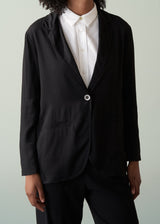 Woman wearing a black relaxed blazer, white shirt and black trousers against a light gray background