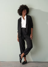 Person wearing a white shirt and black tapered trousers against a plain background