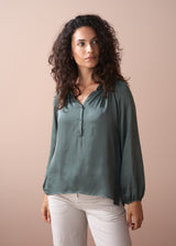 Woman wearing a green blouse and white pants against a beige background