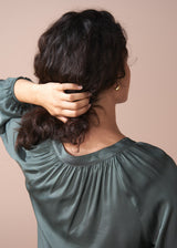 Woman wearing a green blouse and off white wide leg trousers against a beige wall