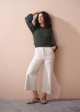 Woman wearing a green blouse and off white wide leg trousers against a beige wall