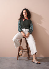 Woman wearing a green blouse and off white wide leg trousers against a beige wall