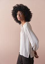 Woman wearing an oatmeal blouse against a beige background