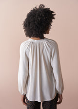 Woman wearing an oatmeal blouse against a beige background
