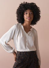 Woman wearing an oatmeal blouse against a beige background