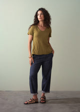 Woman wearing an olive green v-neck cotton t-shirt, paired with blue jeans and sandals