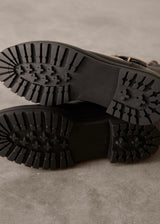 Close-up of black boots with tread pattern on a gray surface