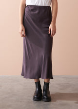 Woman wearing a white t-shirt and dark burgundy satin slip skirt against a beige background