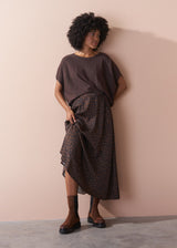 Woman wearing a brown top and patterned skirt against a beige wall.