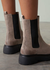 Brown suede boots with black soles on a neutral background