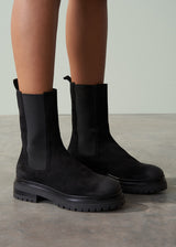 Black Chelsea boots worn by a person on a neutral background