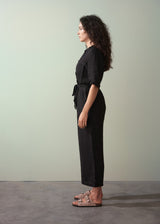 Woman wearing a black jumpsuit standing against a plain background