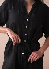 Black button-up linen jumpsuit worn by a person on a beige background