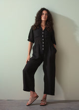 Woman wearing a black linen jumpsuit against a plain background