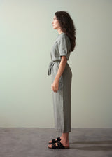 Woman wearing a khaki green linen jumpsuit standing against a plain background