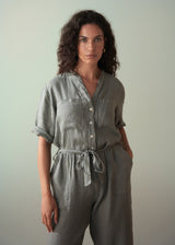 Woman wearing a khaki green linen jumpsuit against a plain background