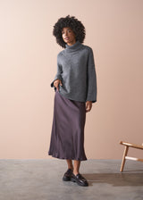 Person wearing a grey chunky knit sweater and satin bias cut skirt against a beige background