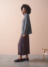 Person wearing a grey chunky knit sweater and satin bias cut skirt against a beige background