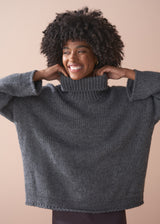 Person wearing a grey chunky knit sweater and satin bias cut skirt against a beige background