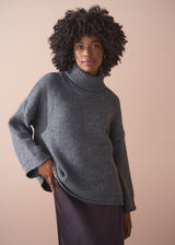 Person wearing a grey chunky knit sweater and satin bias cut skirt against a beige background