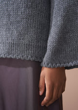 Person wearing a grey chunky knit sweater and satin bias cut skirt against a beige background